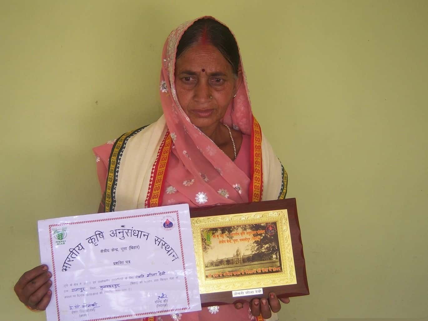 A woman farmer holding a certificate and plaque from an agricultural research institution.