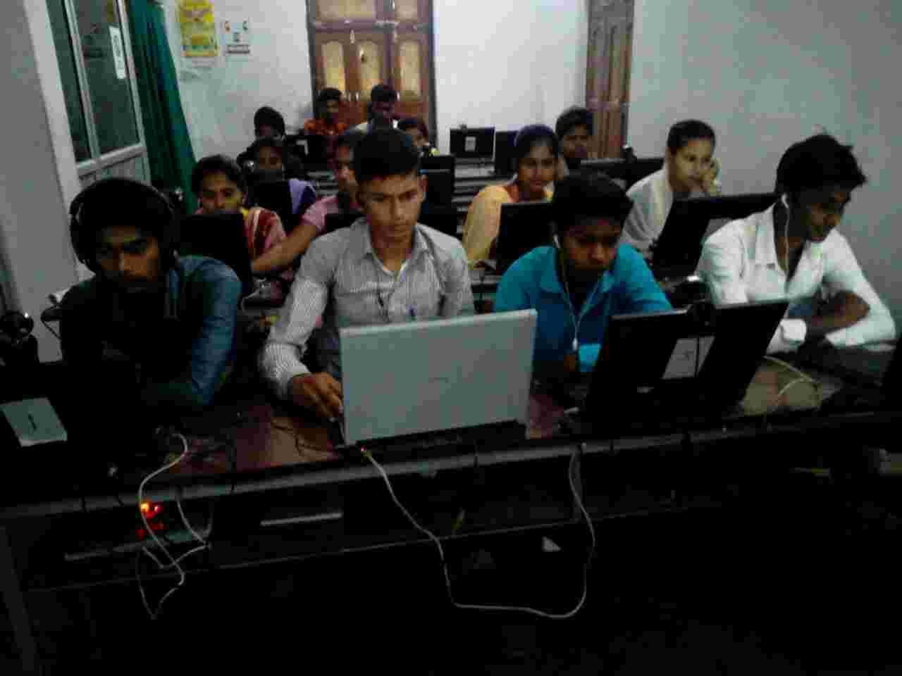 Young people working on laptops in a crowded computer classroom.