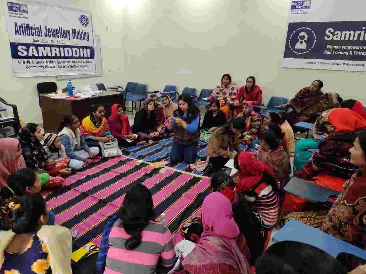 Women seated in a large circle on the floor during an artificial jewellery-making workshop.