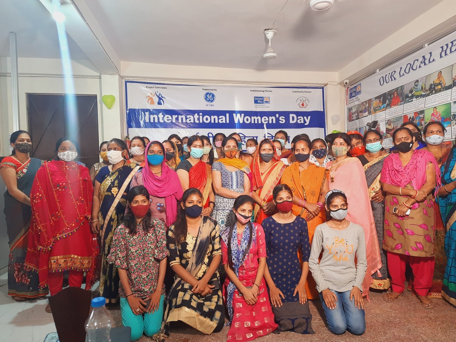 A large group of women and girls standing together indoors at an International Women's Day event.