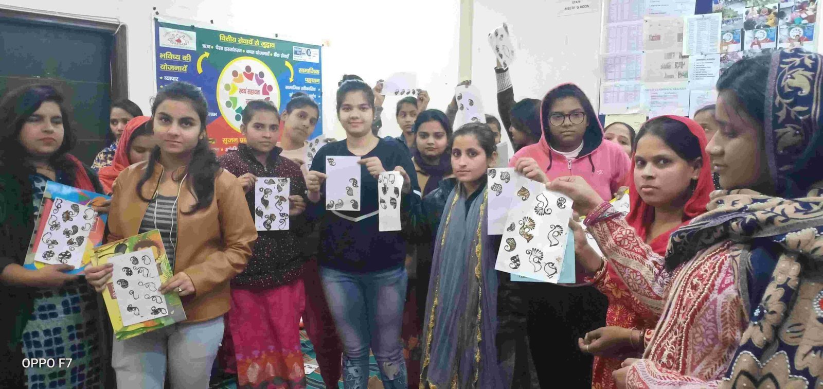 Women standing in a room and holding sheets covered with hand-drawn decorative patterns.