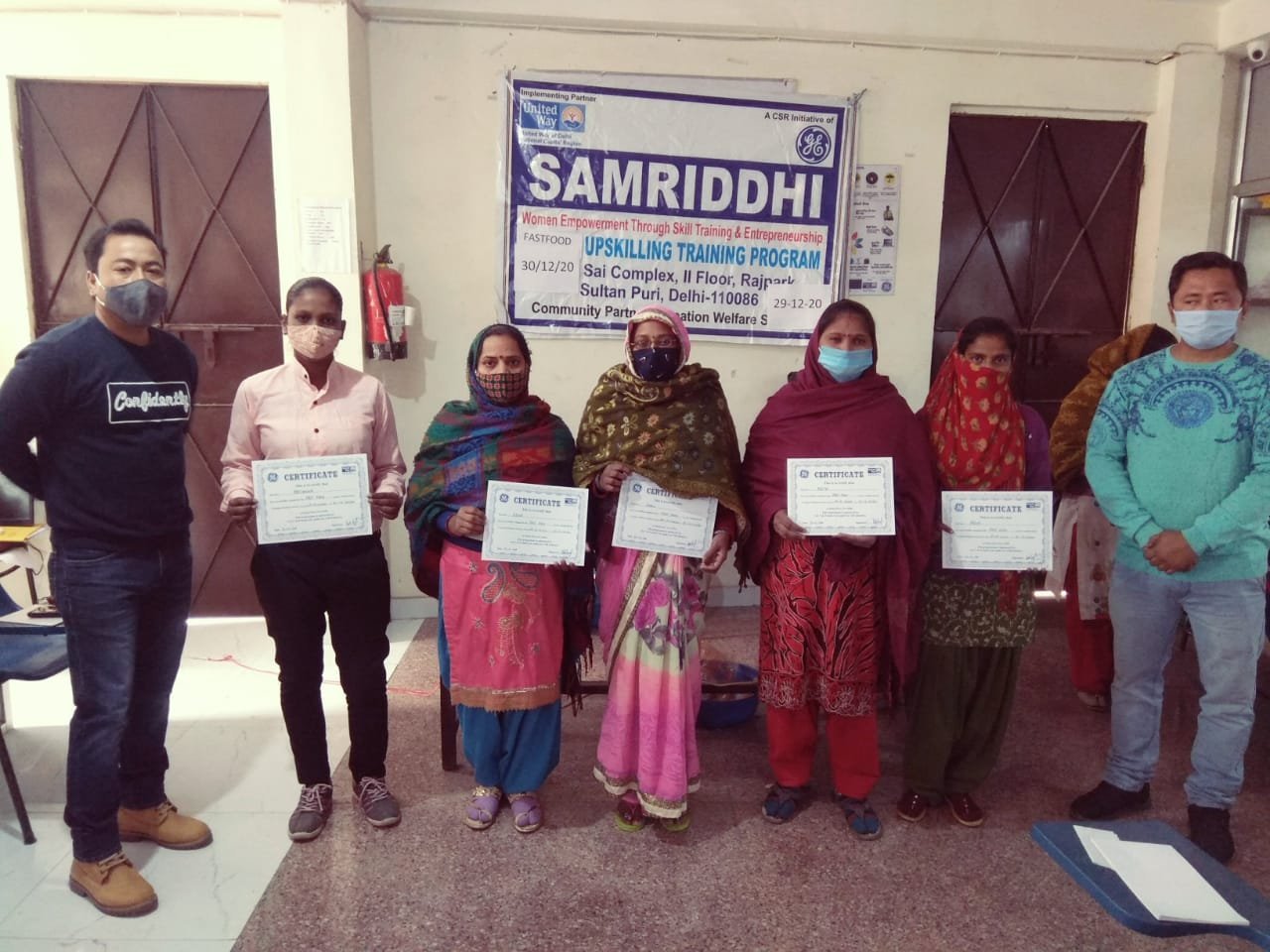 Five women holding training certificates beside two facilitators.