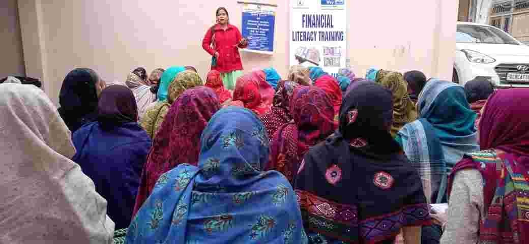 Women seated outdoors during a financial literacy session led by a facilitator.