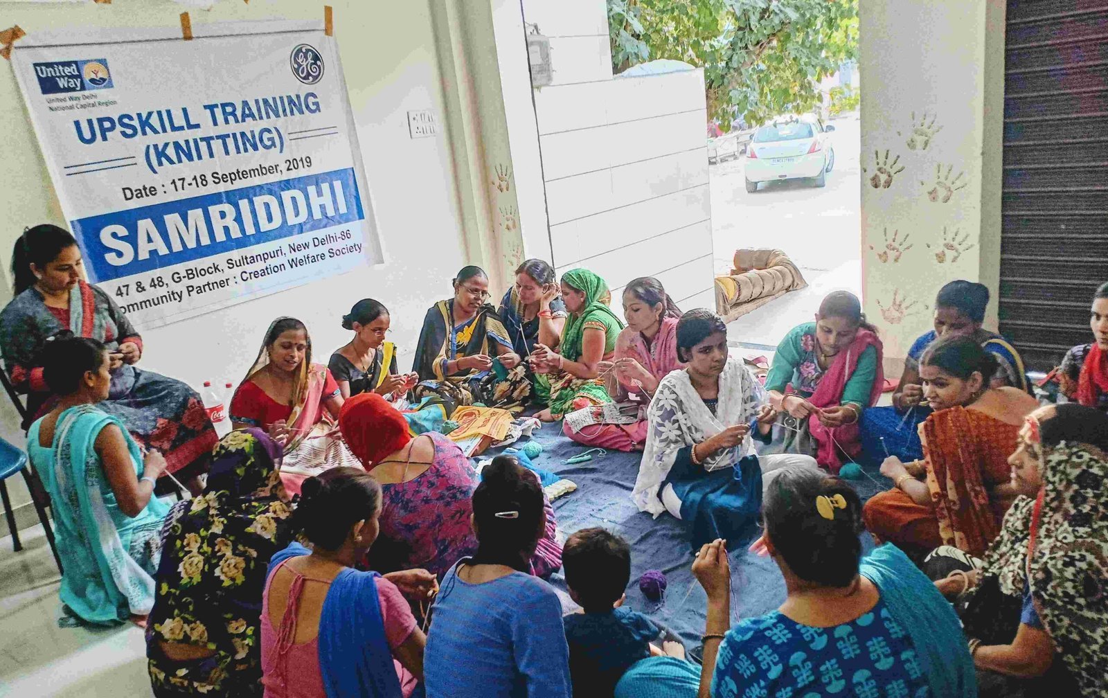 A large group of women seated together and practising knitting with yarn.