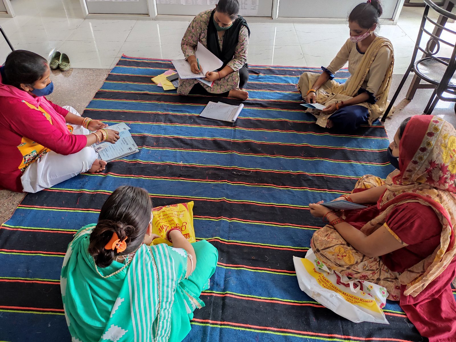 Women seated around a mat with papers during a group meeting.