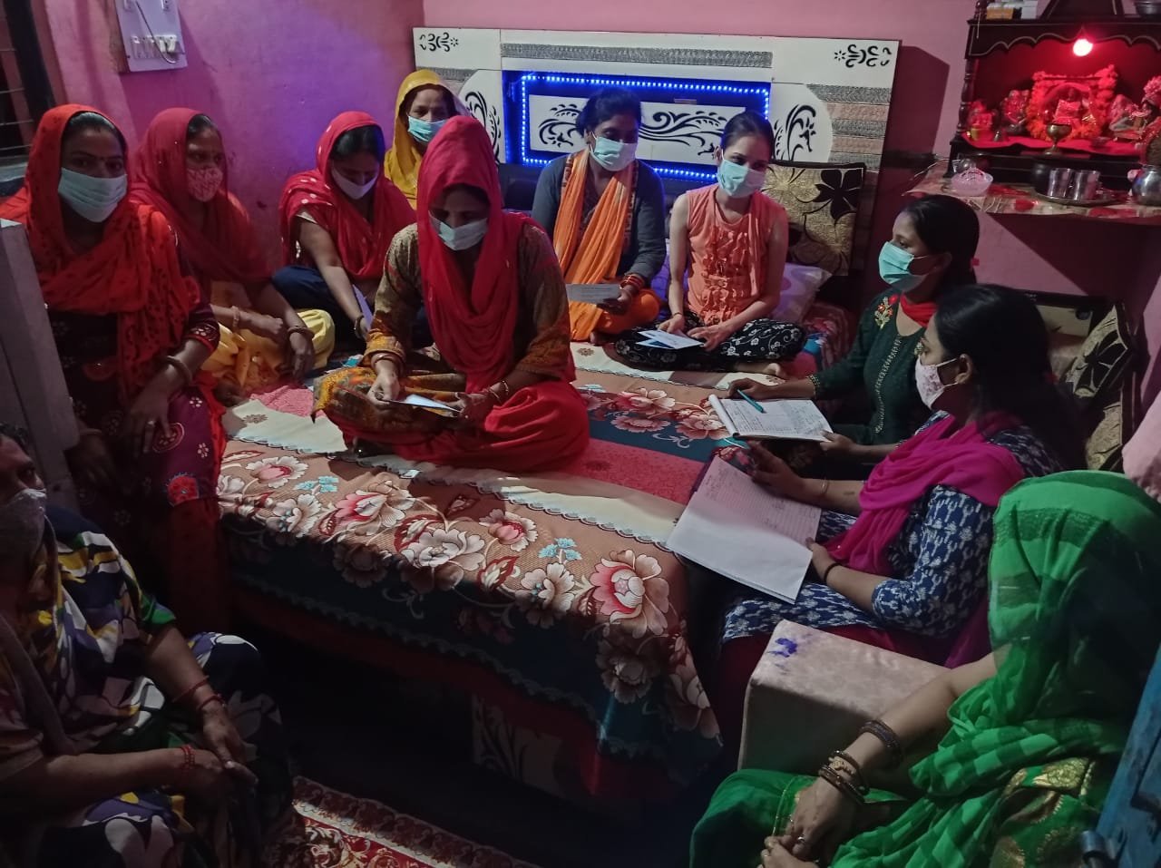 Women seated in a circle with notebooks during a self-help group meeting