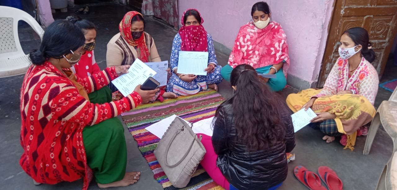 Women seated in a small group and holding printed documents.