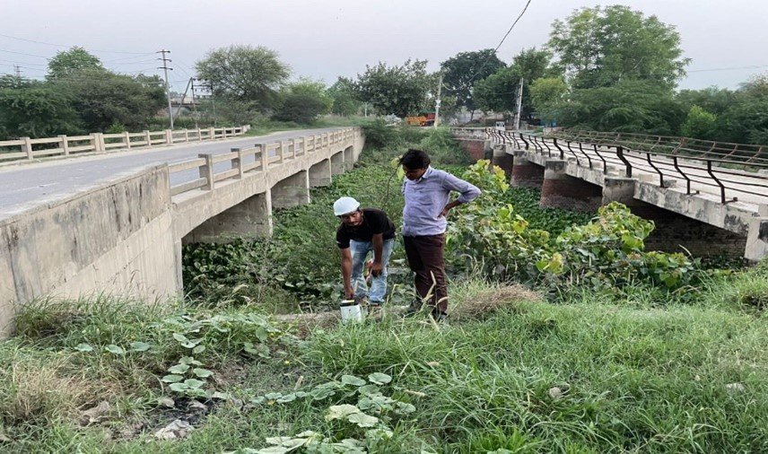 Two field workers inspecting equipment beside a bridge