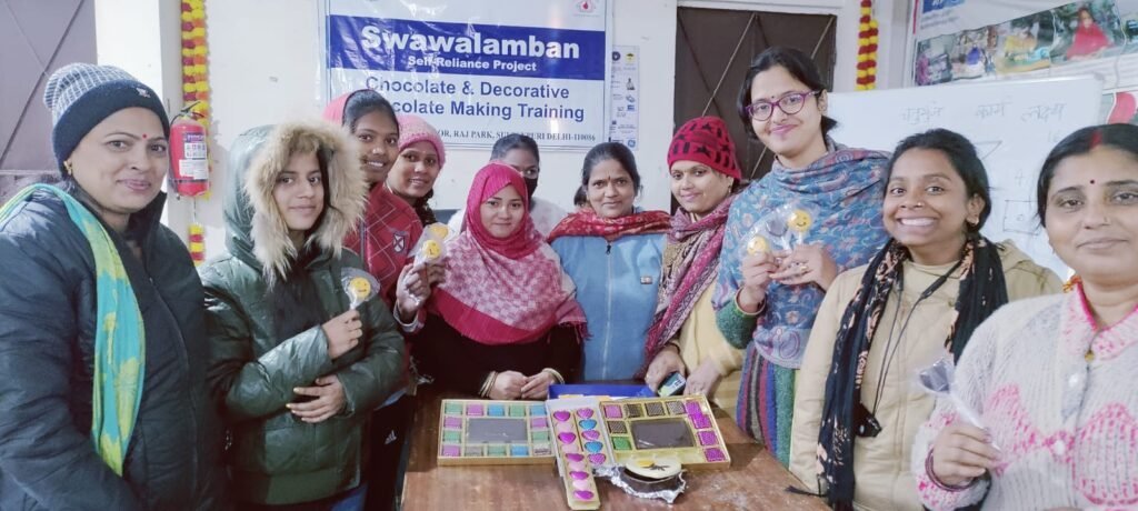 A group of women holding decorated chocolates around a display table after a Swawalamban chocolate-making session.